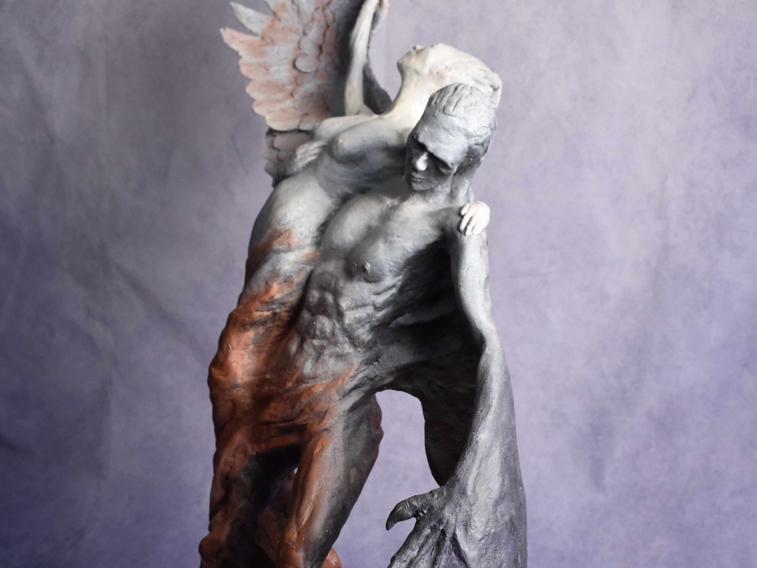 close up crop: figurative sculpture of a man and woman rising from a swirl. man has a devil wing, woman has an angel wing.