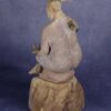 three quarters back view: clay sculpture of seated woman with a branch for an arm and coral protruding from her head like a crown.