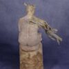 Back view: clay sculpture of seated woman with a branch for an arm and coral protruding from her head like a crown.