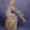 right side view: clay sculpture of seated woman with a branch for an arm and coral protruding from her head like a crown.